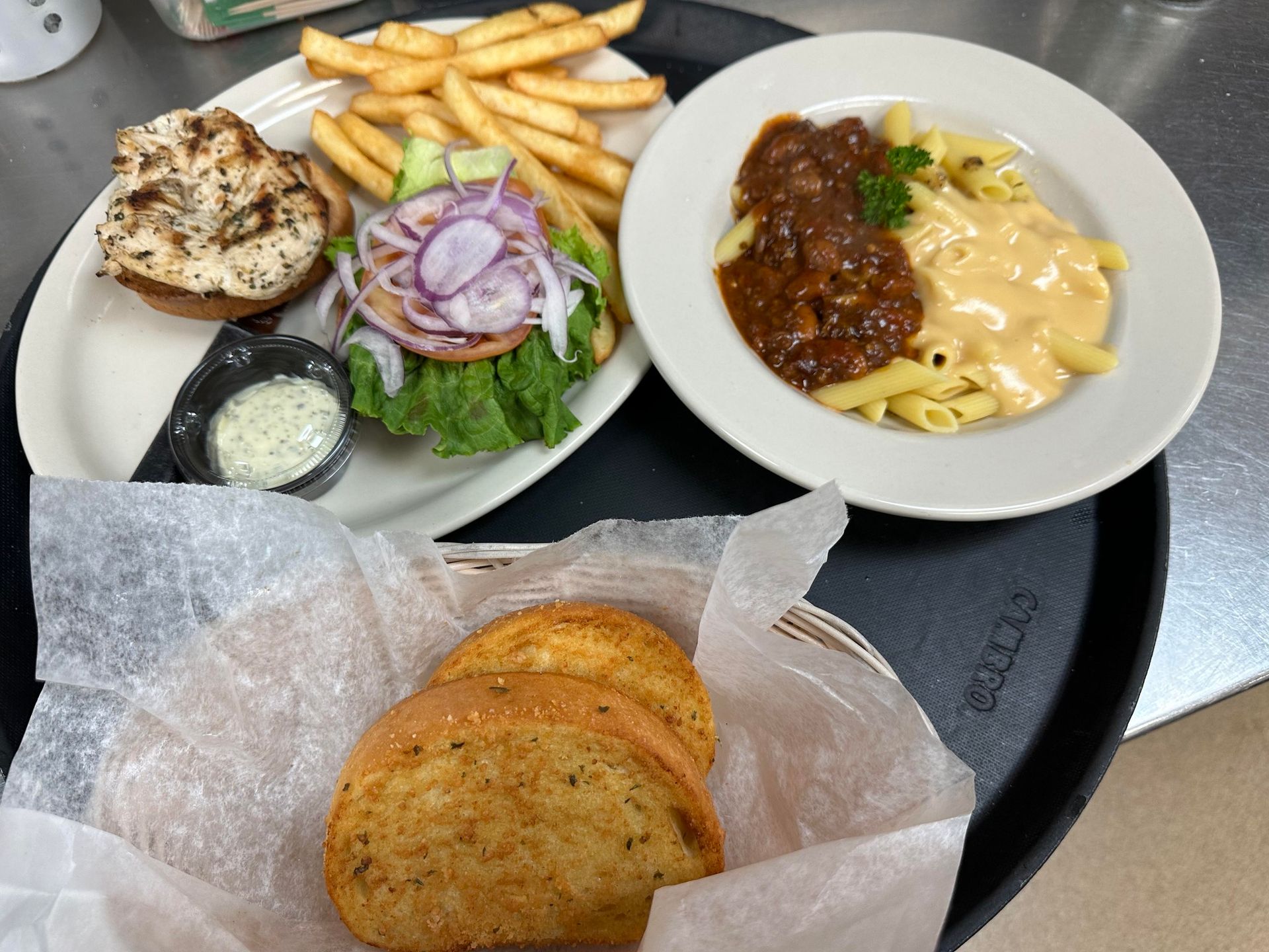 Tray with a grilled chicken sandwich, fries, pasta with sauce, and garlic bread.