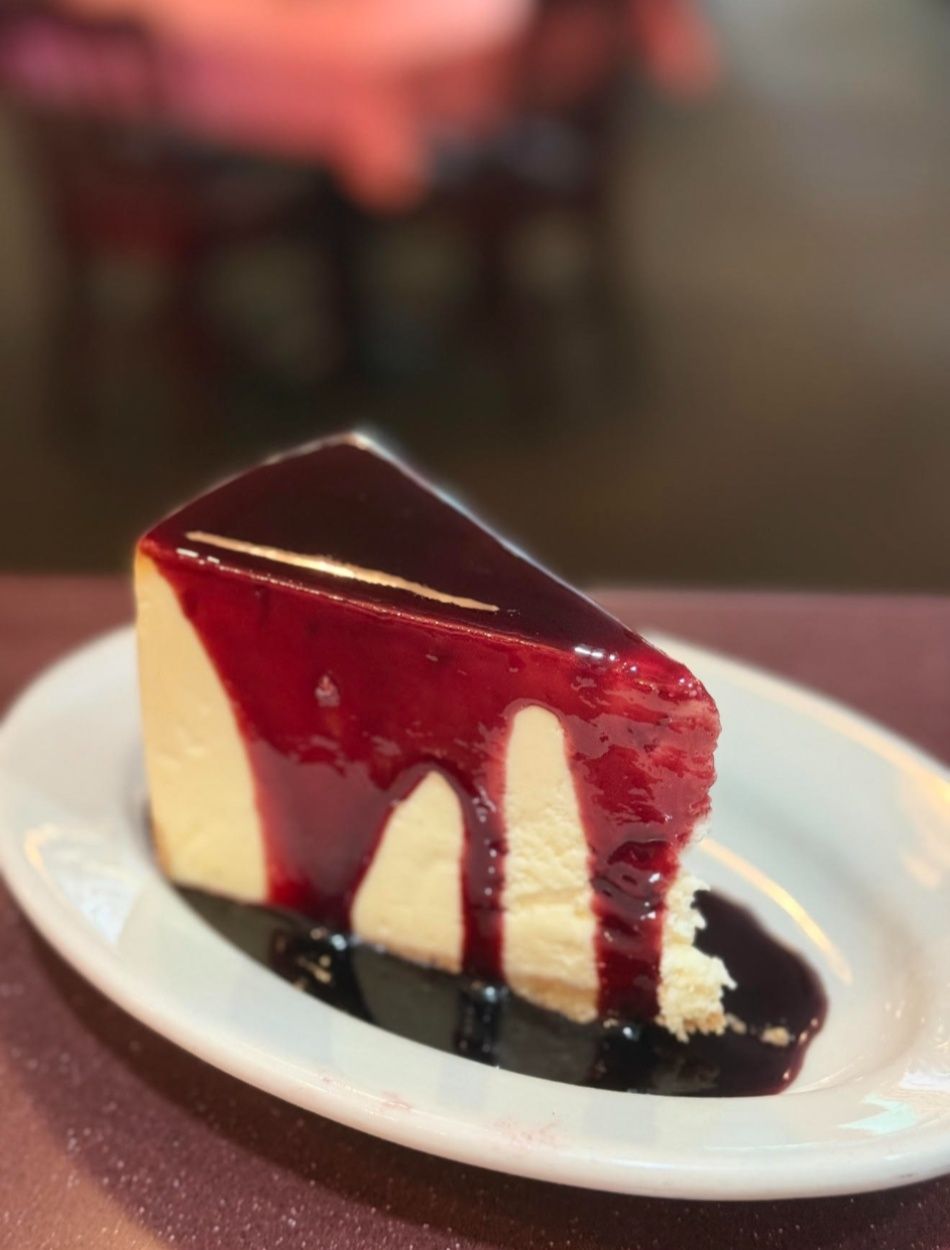 Slice of cheesecake with red berry sauce on a white plate.