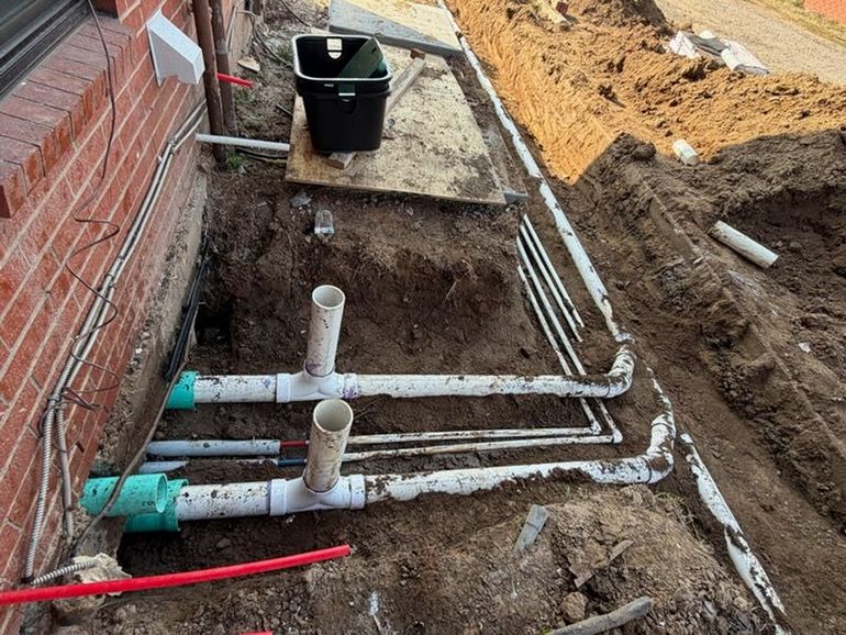 Under-sink plumbing showing a white P-trap, copper pipes, a brass valve, and an open drainage hose connector.