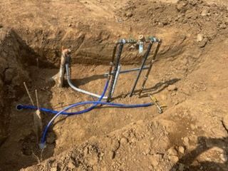Underground utility pipes and blue cables exposed in a dirt trench
