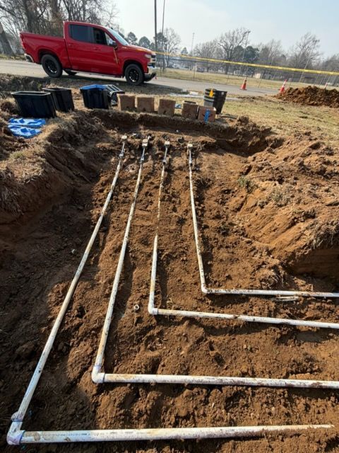Underground PVC pipes installed in a dirt trench at a construction site, with a red truck nearby.