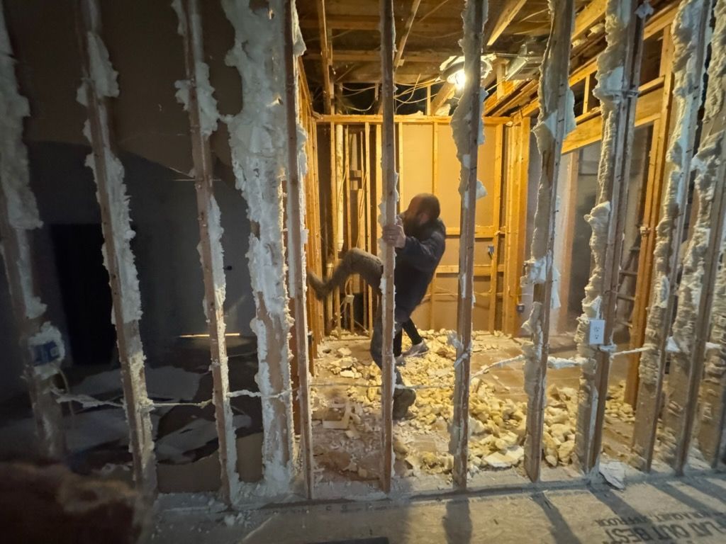 Construction workers framing interior walls in a house under renovation, with insulation and exposed studs.