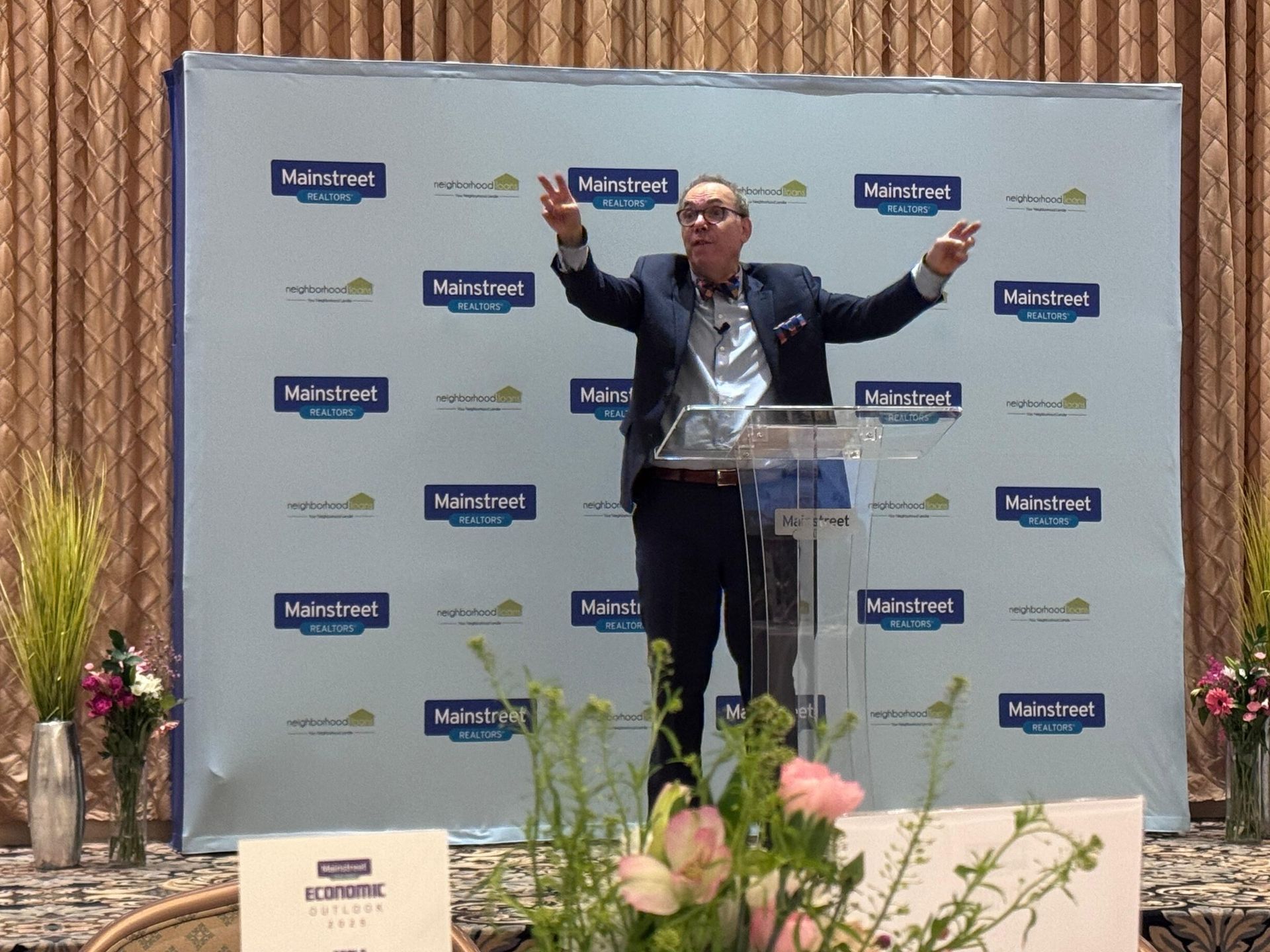 A man in a suit is standing at a podium with his arms outstretched.
