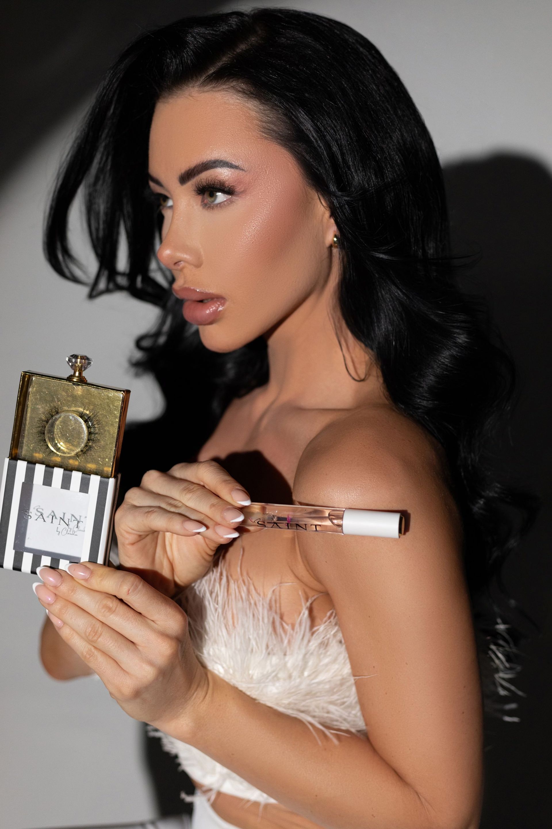 A woman in a white top is holding lip gloss in her hand.