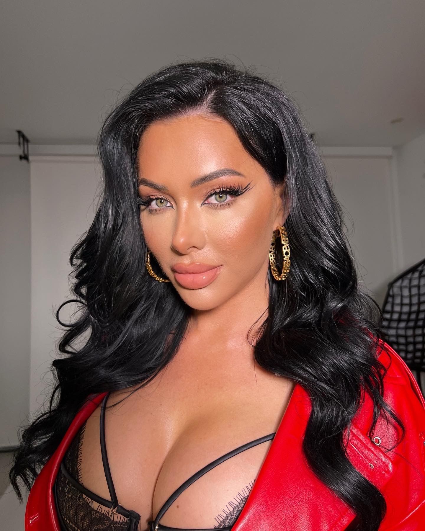 A woman with long black hair is wearing a red jacket and earrings.