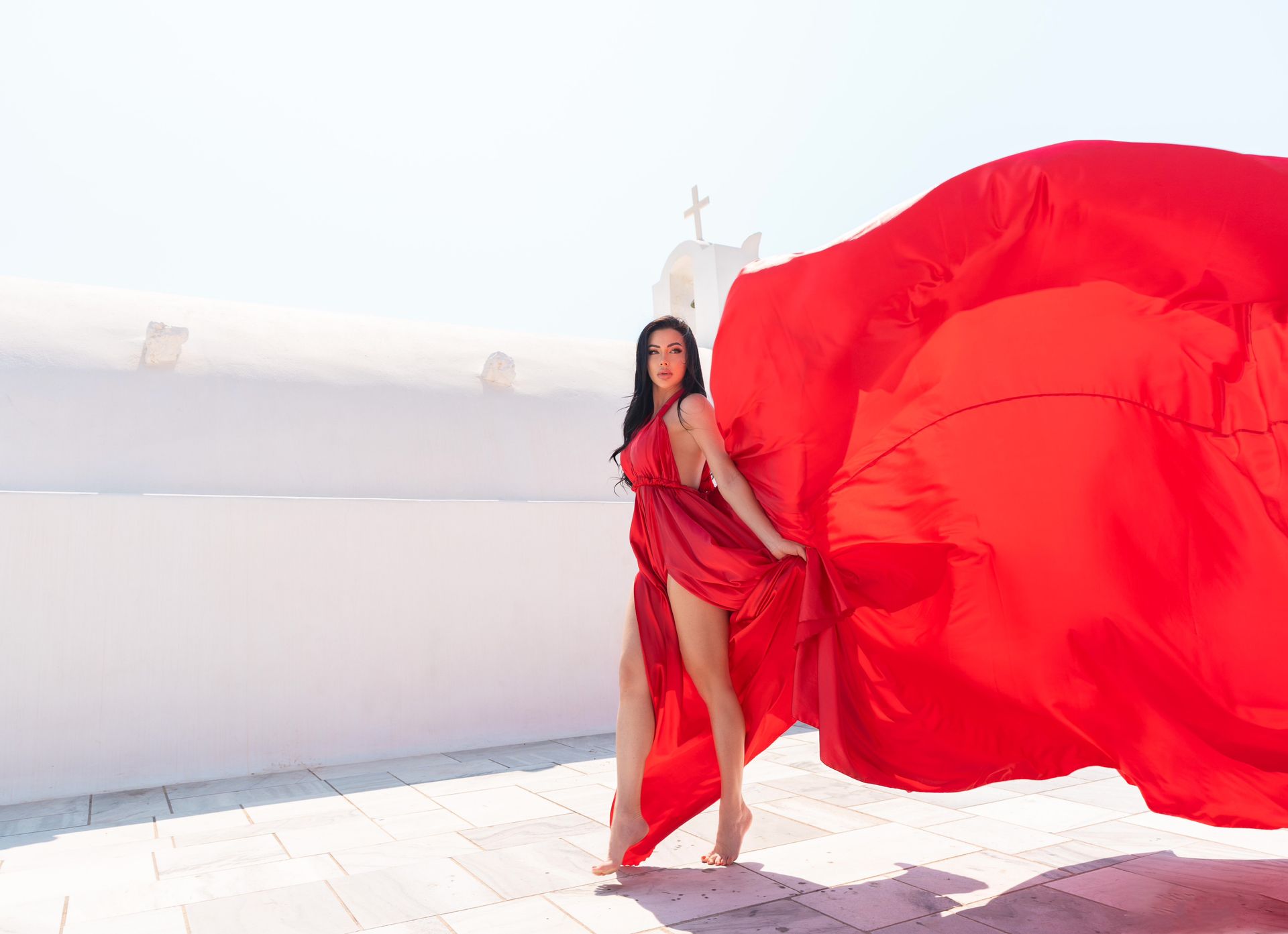 A woman in a long red dress is standing in front of a white building.