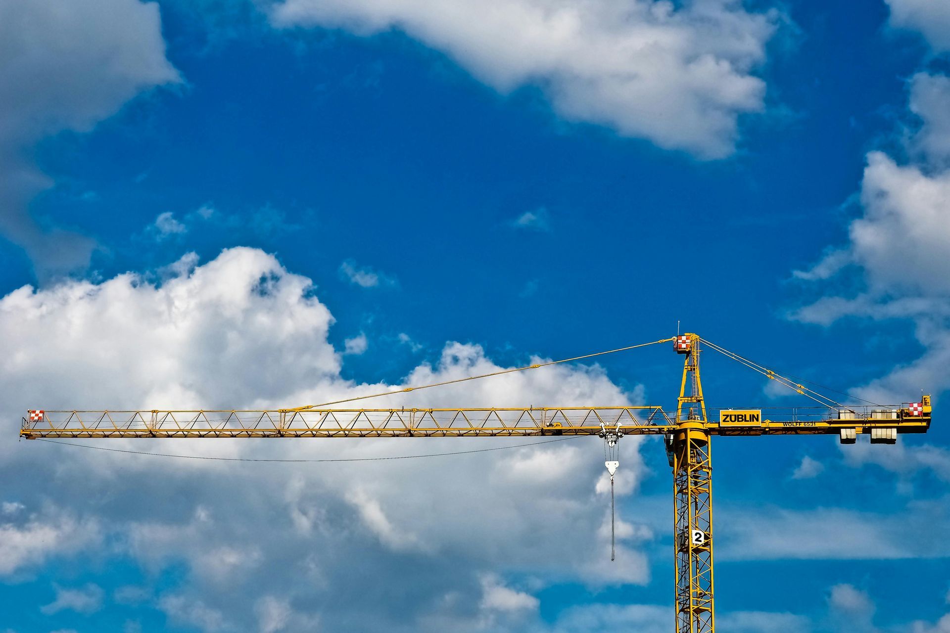 A yellow construction crane is against a blue sky with clouds.