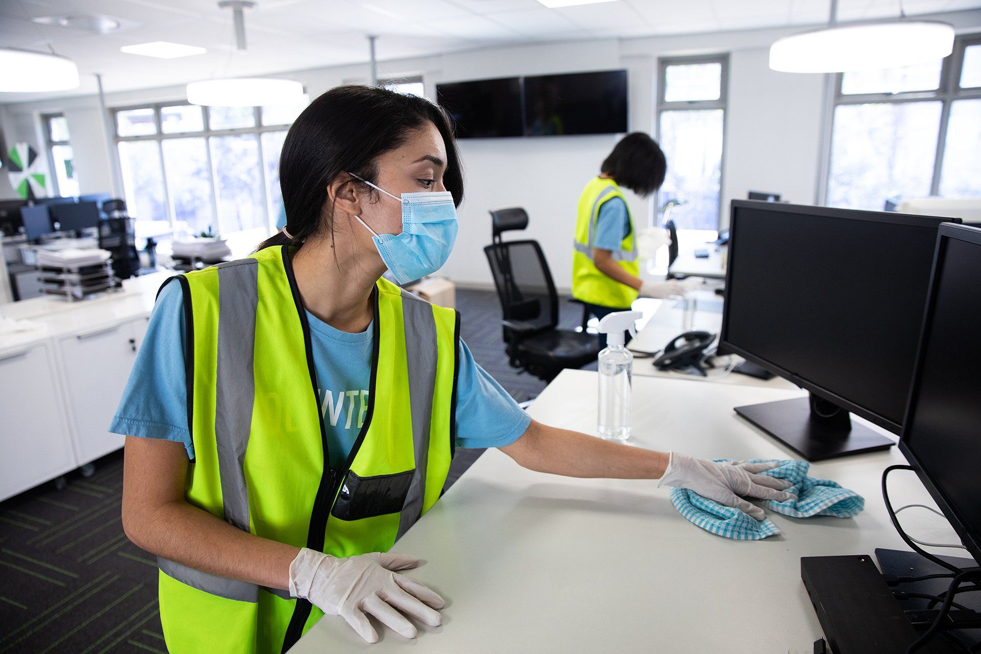 Office cleaning Exeter of a team wearing hi vis vests, gloves and face masks sanitizing an office using disinfectant. Hygiene in workplace during Coronavirus Covid 19 pandemic.