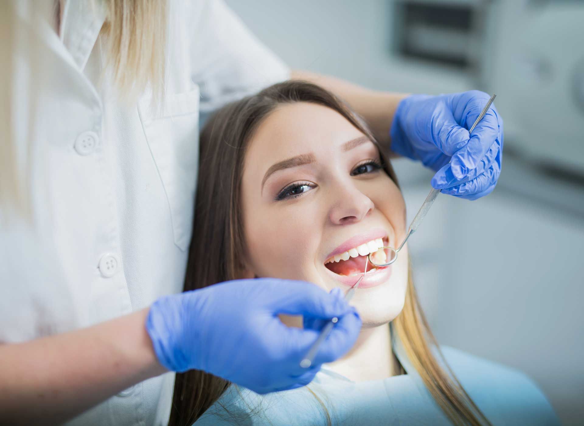 Dentist examining a patient's teeth with dental instruments; the patient is smiling.