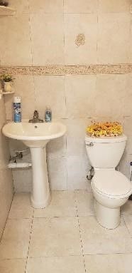 Picture of white tiled bathroom, with orange flowers sitting atop the toilet.