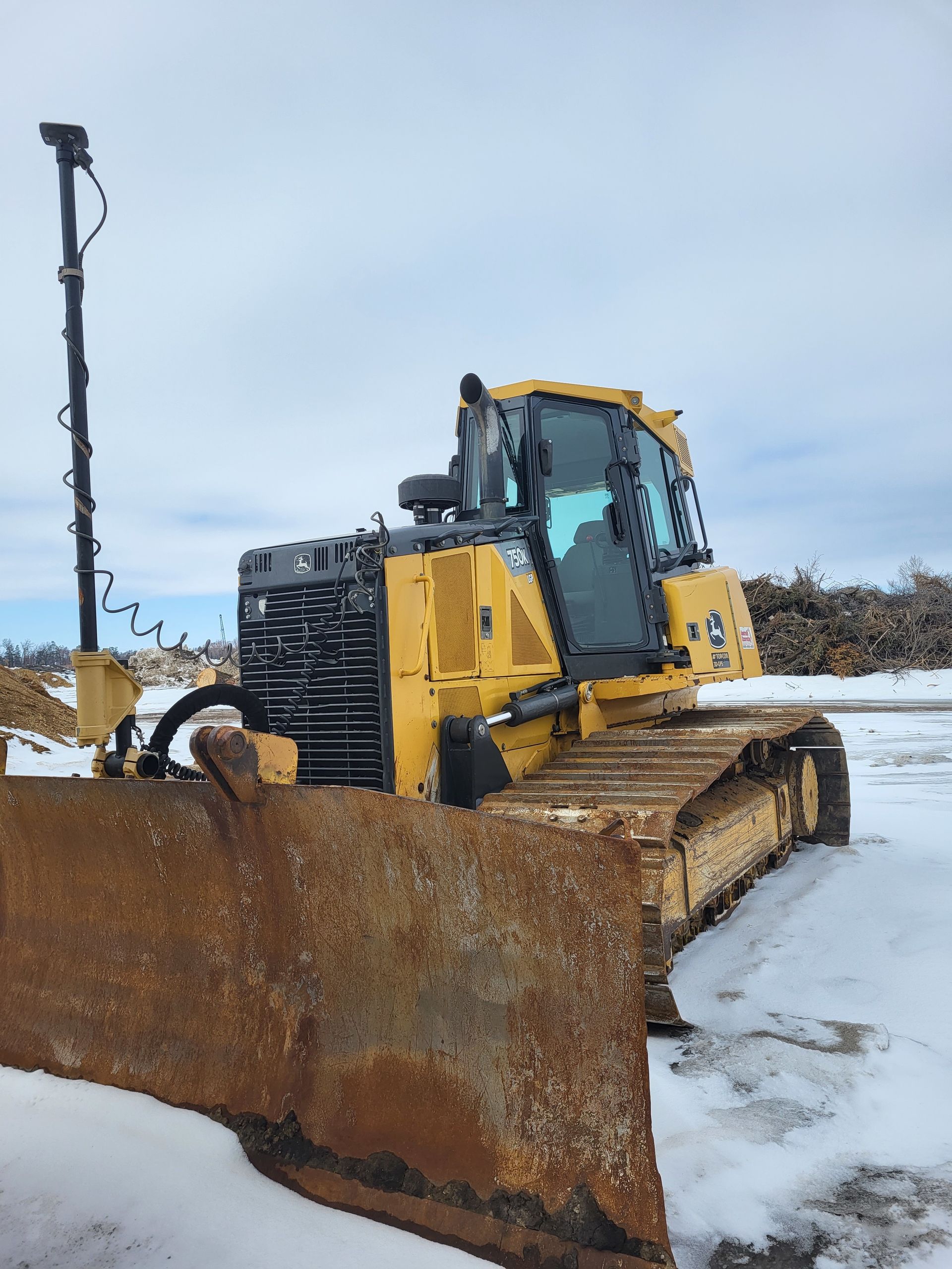 A yellow Caterpillar bulldozer with a GPS mast attached to its blade, parked on snow-covered ground.