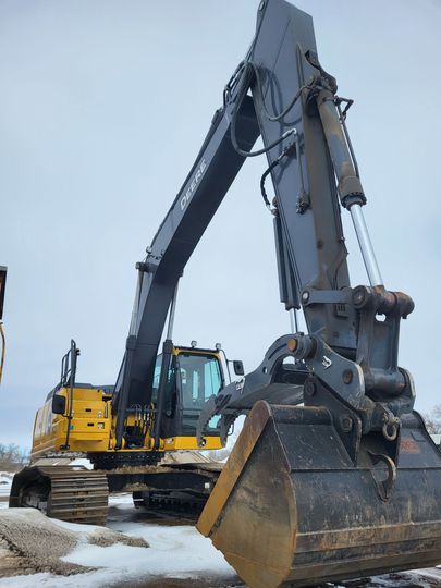 A yellow and grey industrial excavator with a large bucket arm, parked on a snowy ground under an overcast sky.