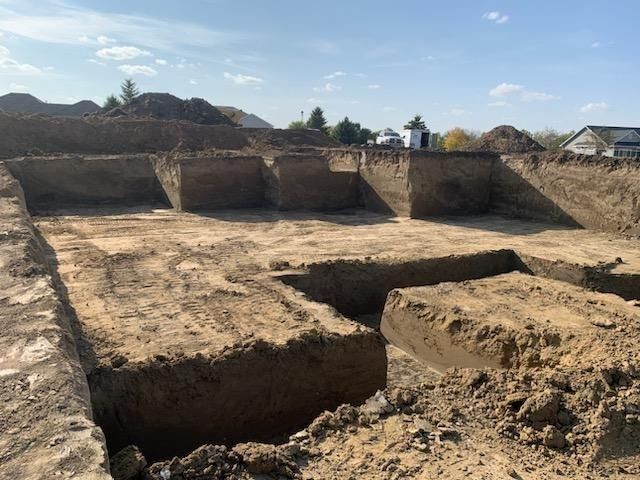 A wide, deep dirt excavation site prepared for a building foundation under a clear blue sky.
