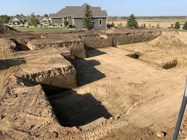 An excavation site for a home foundation showing dirt trenches in a residential development under a clear blue sky.