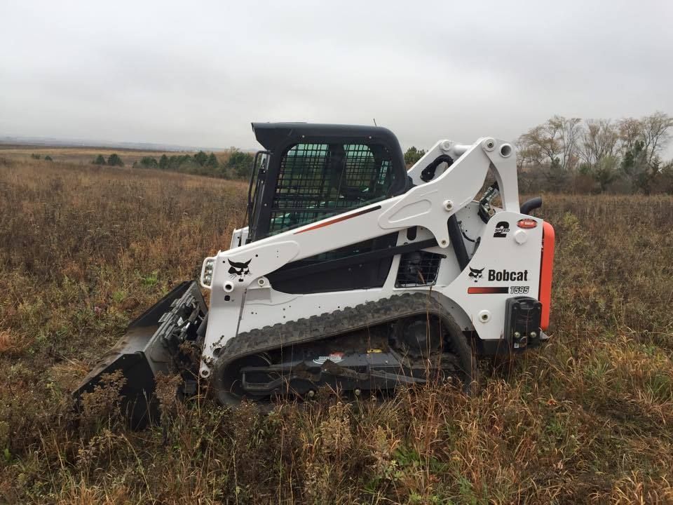 A white Bobcat compact track loader sits in an open, grassy field under a cloudy, overcast sky.