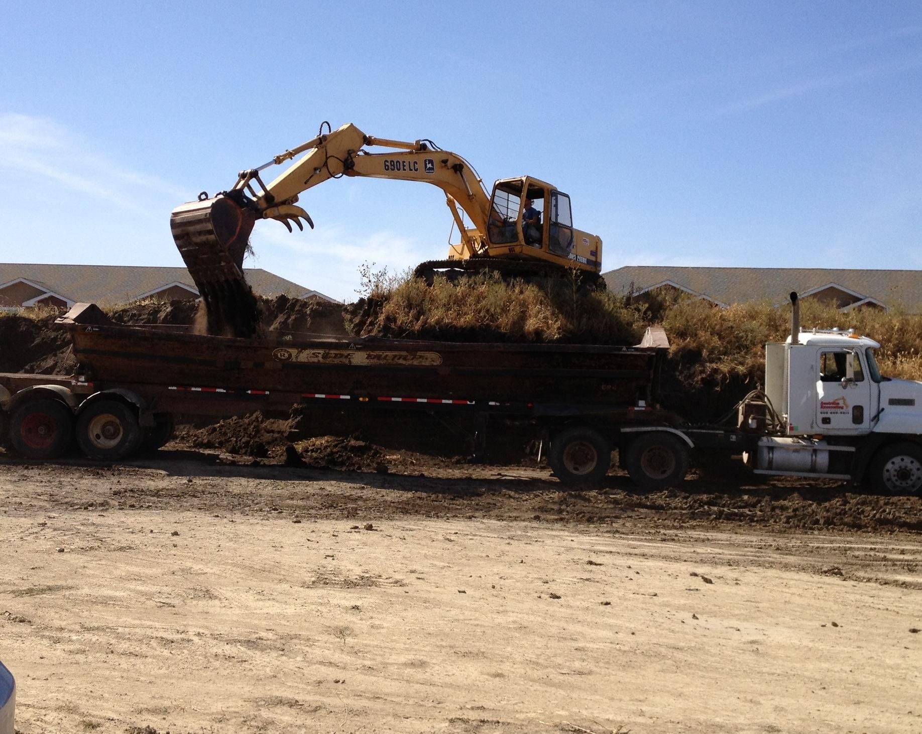 A yellow excavator loads dirt into a white dump truck at an outdoor construction site.