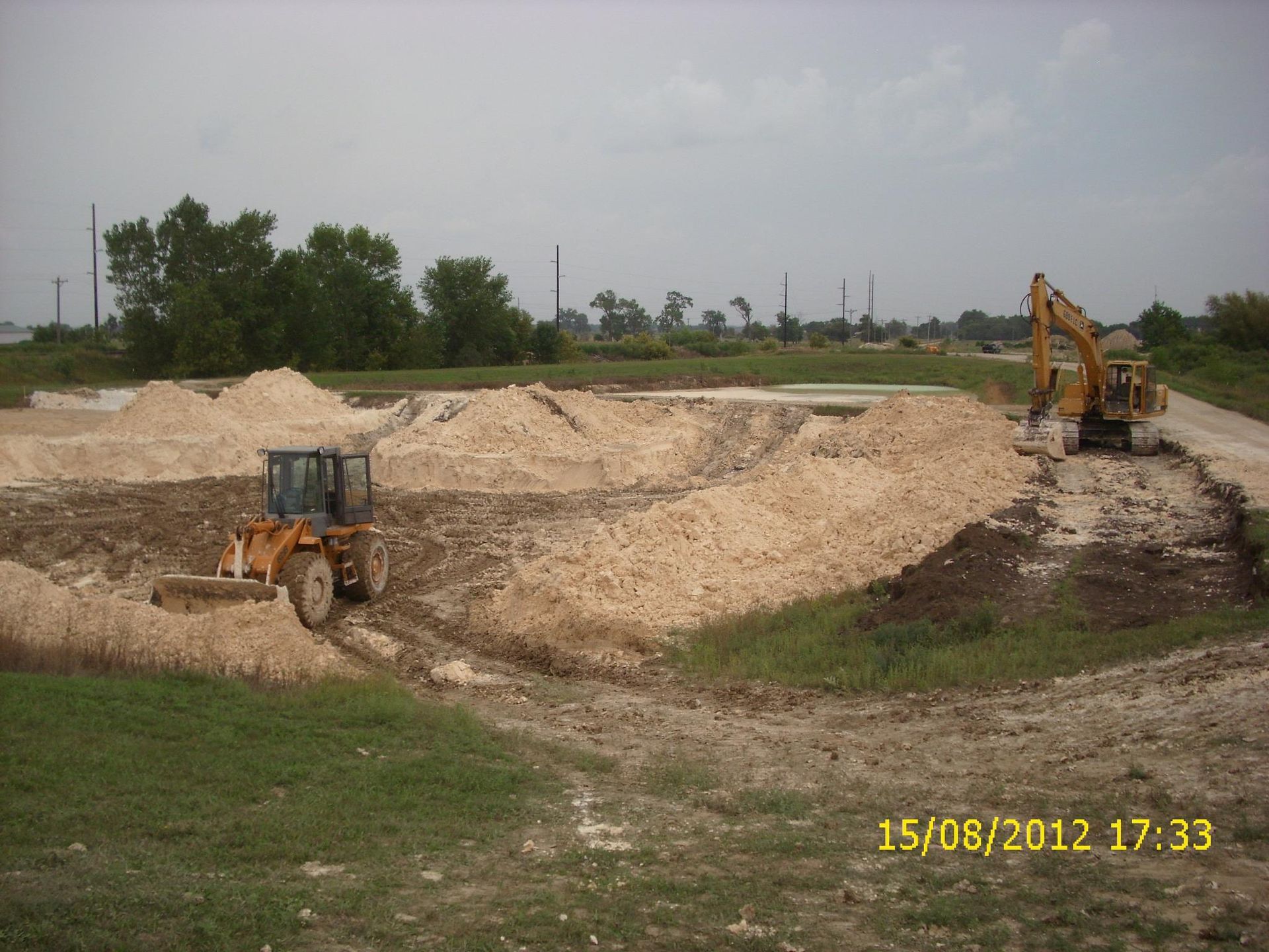 Construction site with a yellow bulldozer and an excavator working in an open field, creating mounds of dirt and sand.