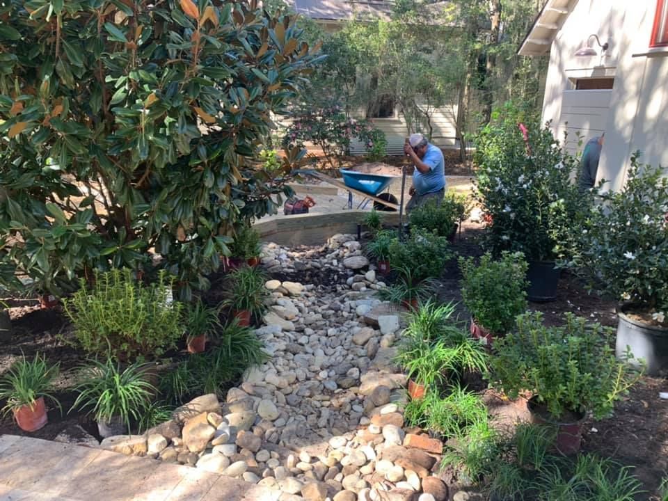 A man shovels in a garden bed with a stone-filled dry creek bed.