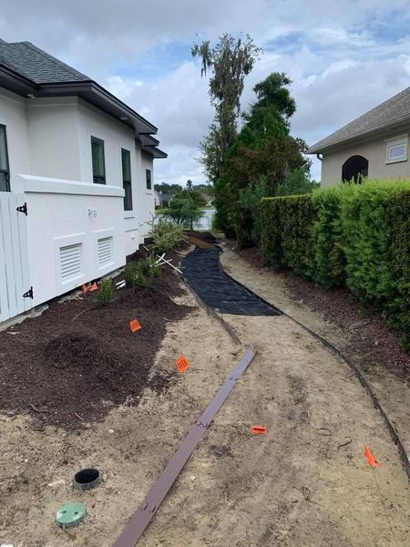 Pathway being landscaped with dark mulch and weed barrier, between two houses.