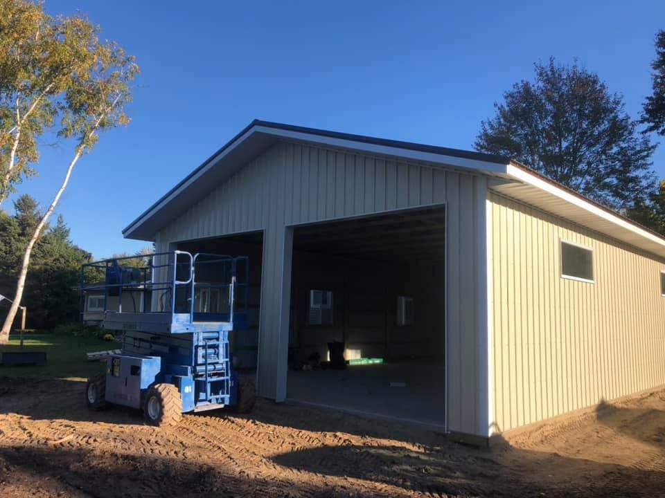 New beige metal-sided two-car garage under construction; blue lift in front, blue sky.