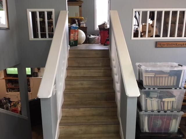 Staircase with white railing leads upwards; gray walls with window and storage bins on the right.