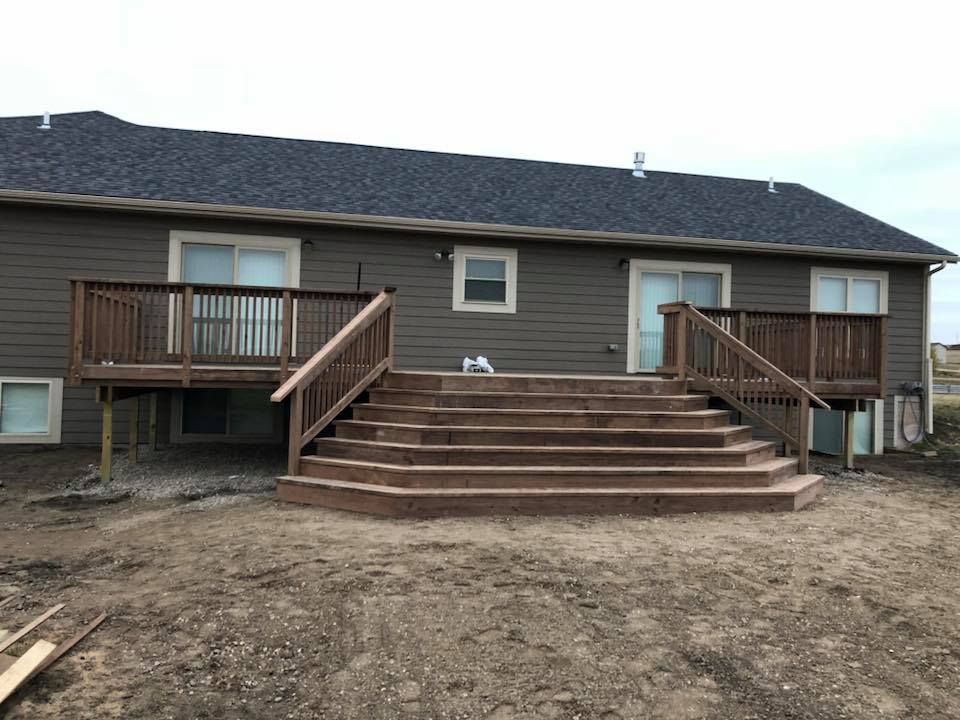 Brown deck with steps leading down to a dirt yard, attached to a brown house with sliding glass doors.