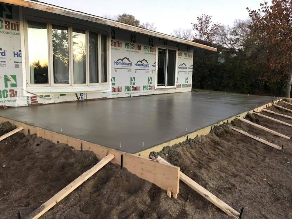 Concrete patio being built next to a house with large windows.