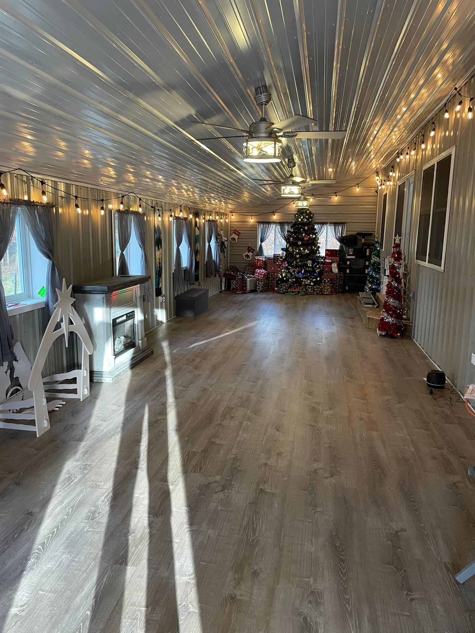 Empty room with wooden floors, decorated for Christmas. Fairy lights, tree, and presents.