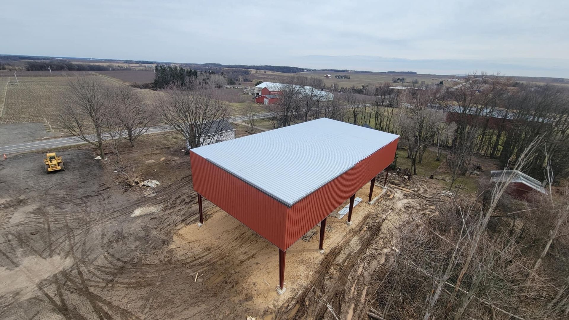 Red barn with silver roof on stilts in a rural landscape; cloudy sky.