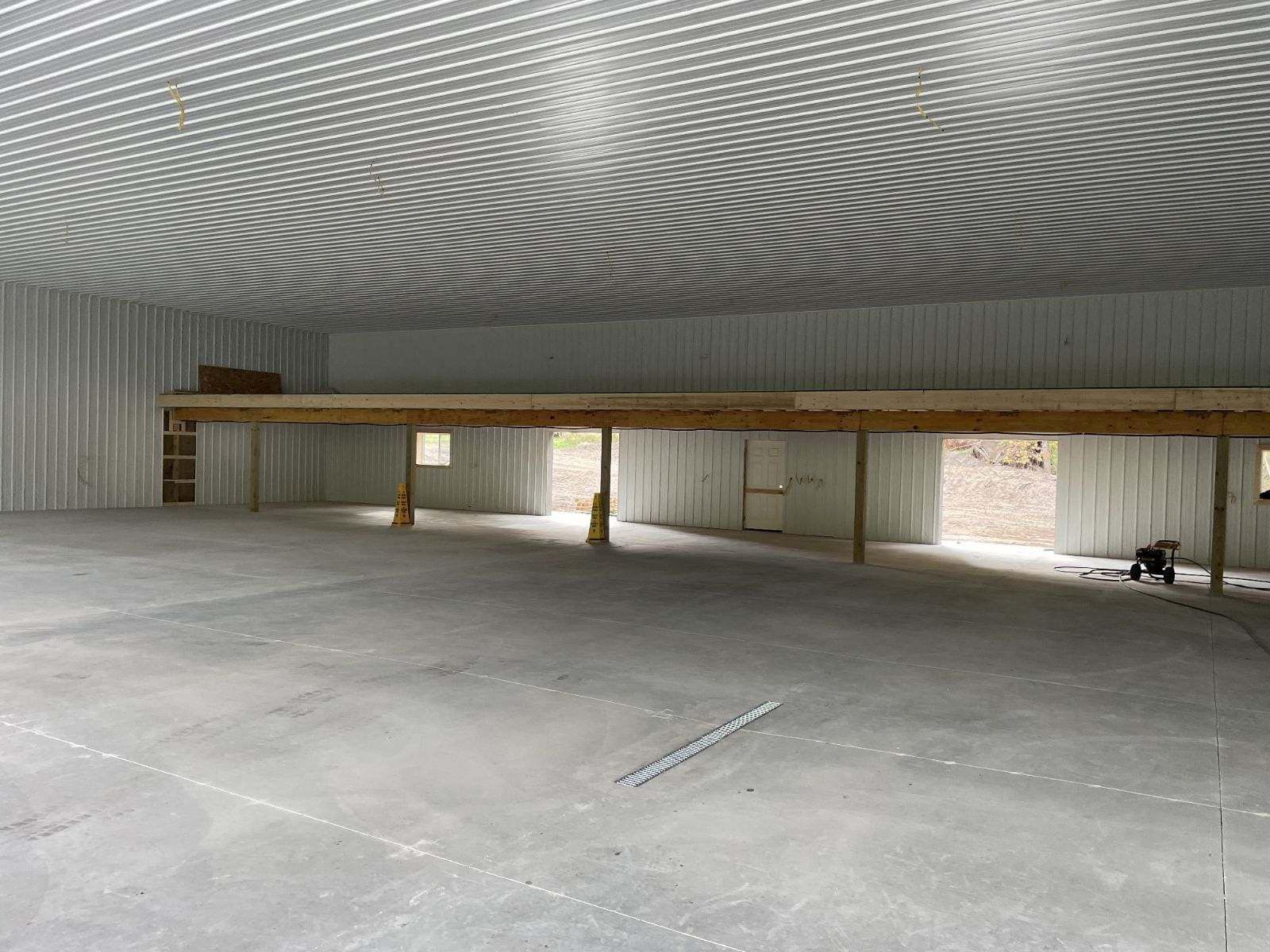 Interior of a large, unfinished building with a concrete floor and a wooden mezzanine.