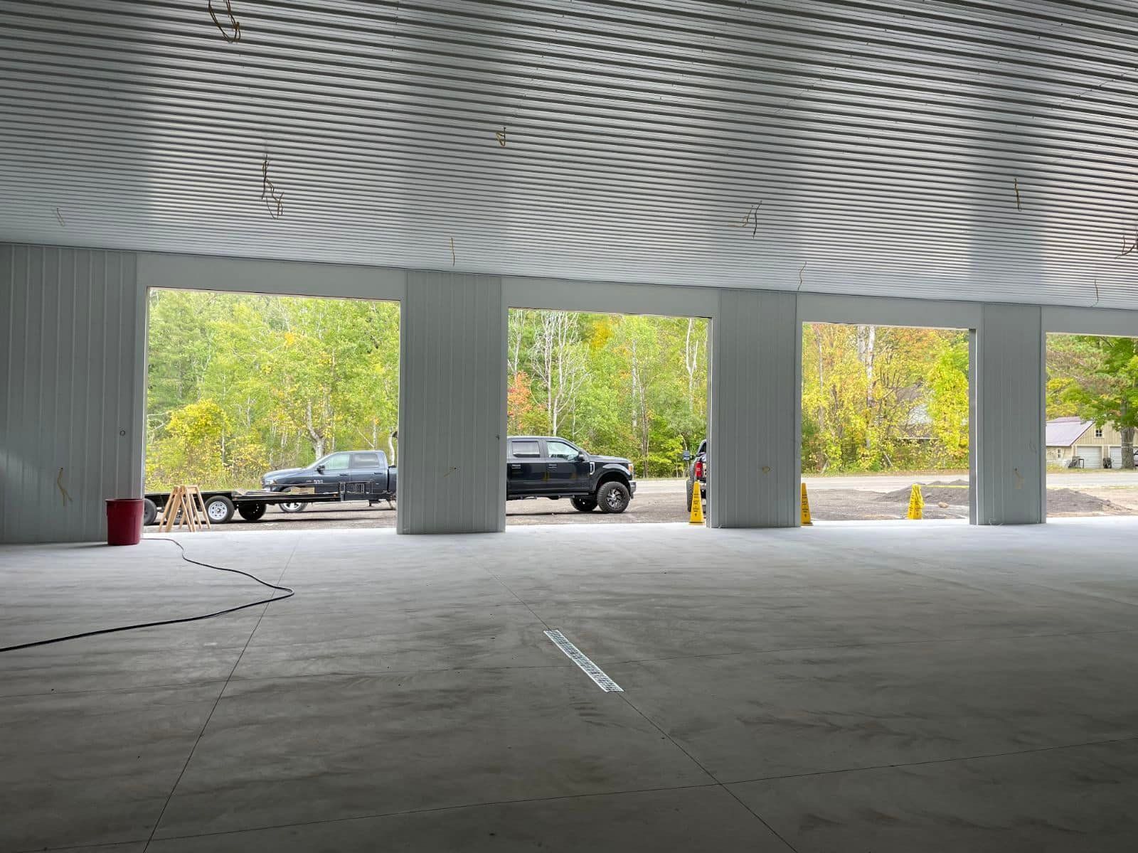 Interior view of a garage with open bays. Two trucks are visible outside, with trees and a green background.