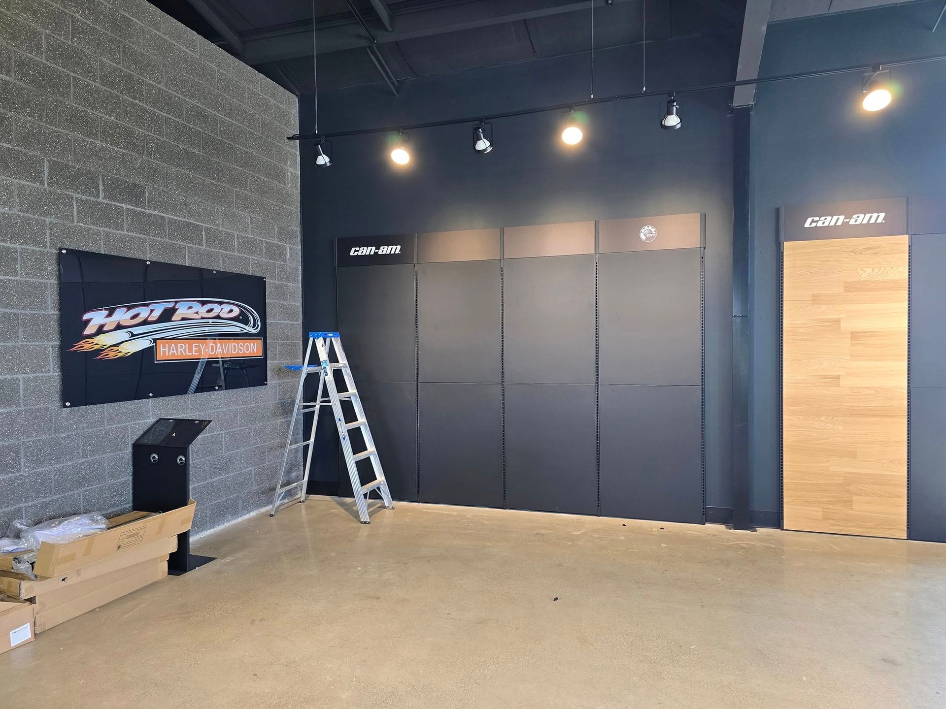 Interior of a showroom with gray brick and dark gray walls. A ladder leans against the wall, with track lighting.