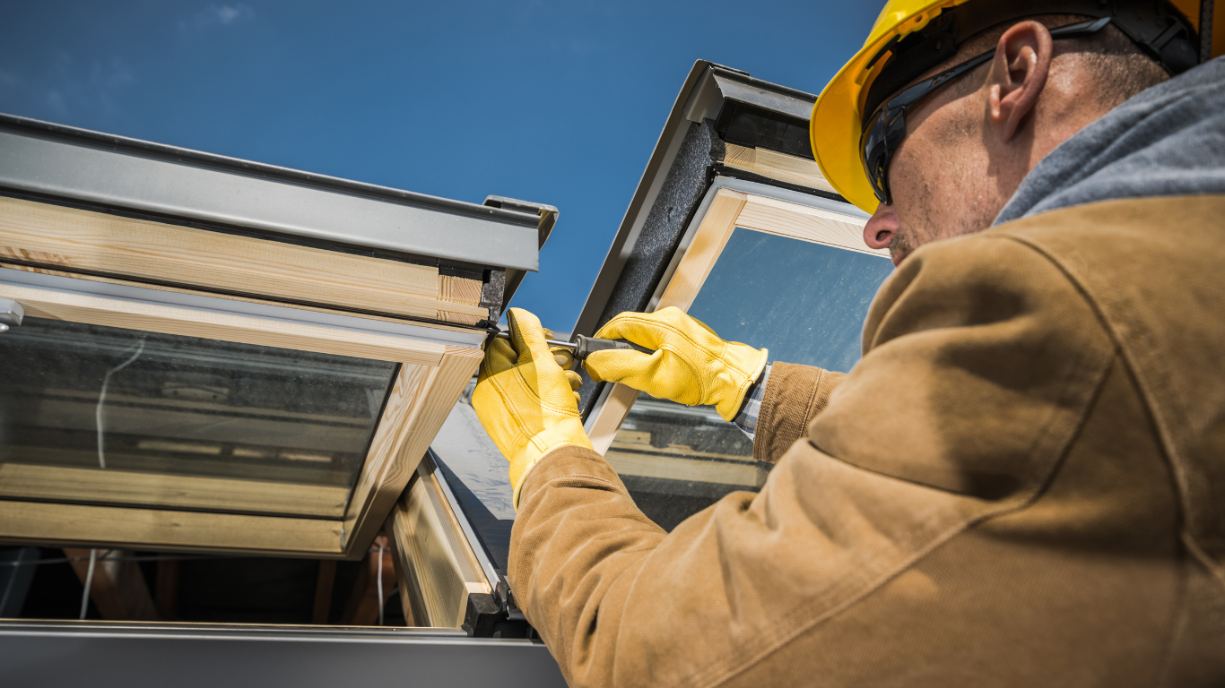 Construction worker in yellow gloves and hard hat installing a skylight on a rooftop.