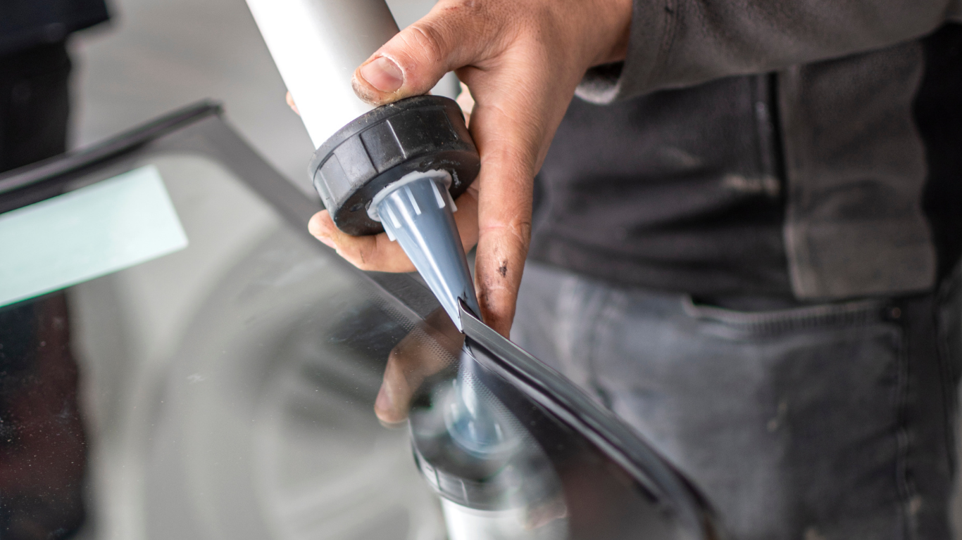 A person applying sealant from a caulking gun to a windshield.