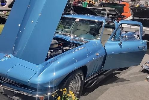 Blue vintage Corvette with the hood and door open, displayed at a car show.