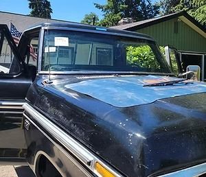 Black Ford pickup truck with weathered paint, parked outside a house with an American flag in the background.