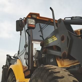 Yellow construction loader with black arm and tire against a cloudy sky.