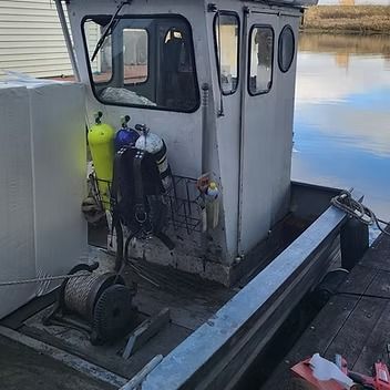 A white work boat with scuba gear hanging on the side, docked on a waterway.