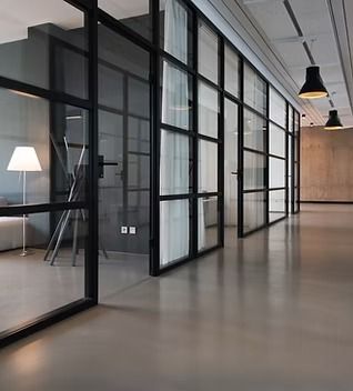 Modern office interior with glass-walled rooms and black frames. Polished gray floors and pendant lights.