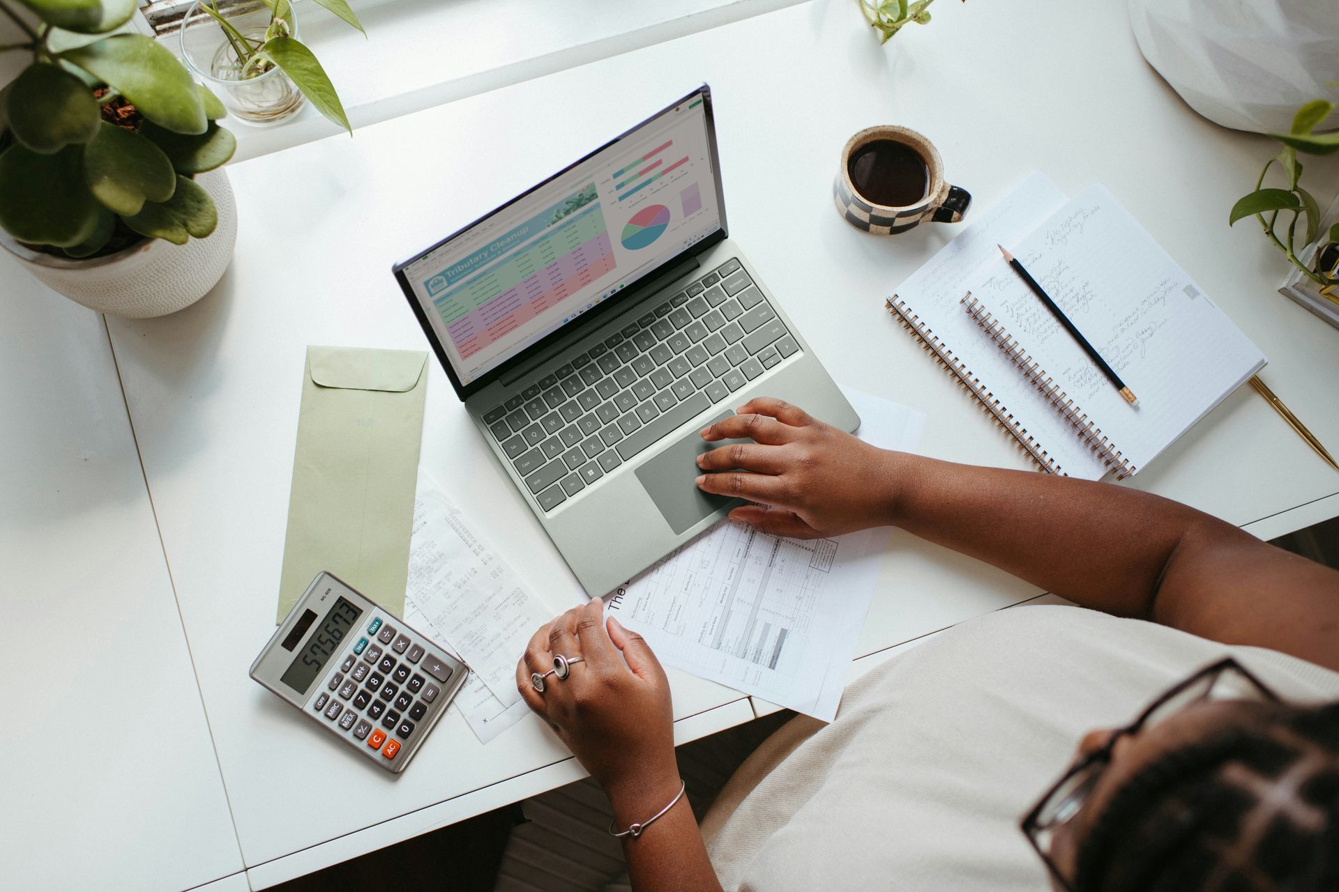 Person working at desk with laptop, calculator, and documents.