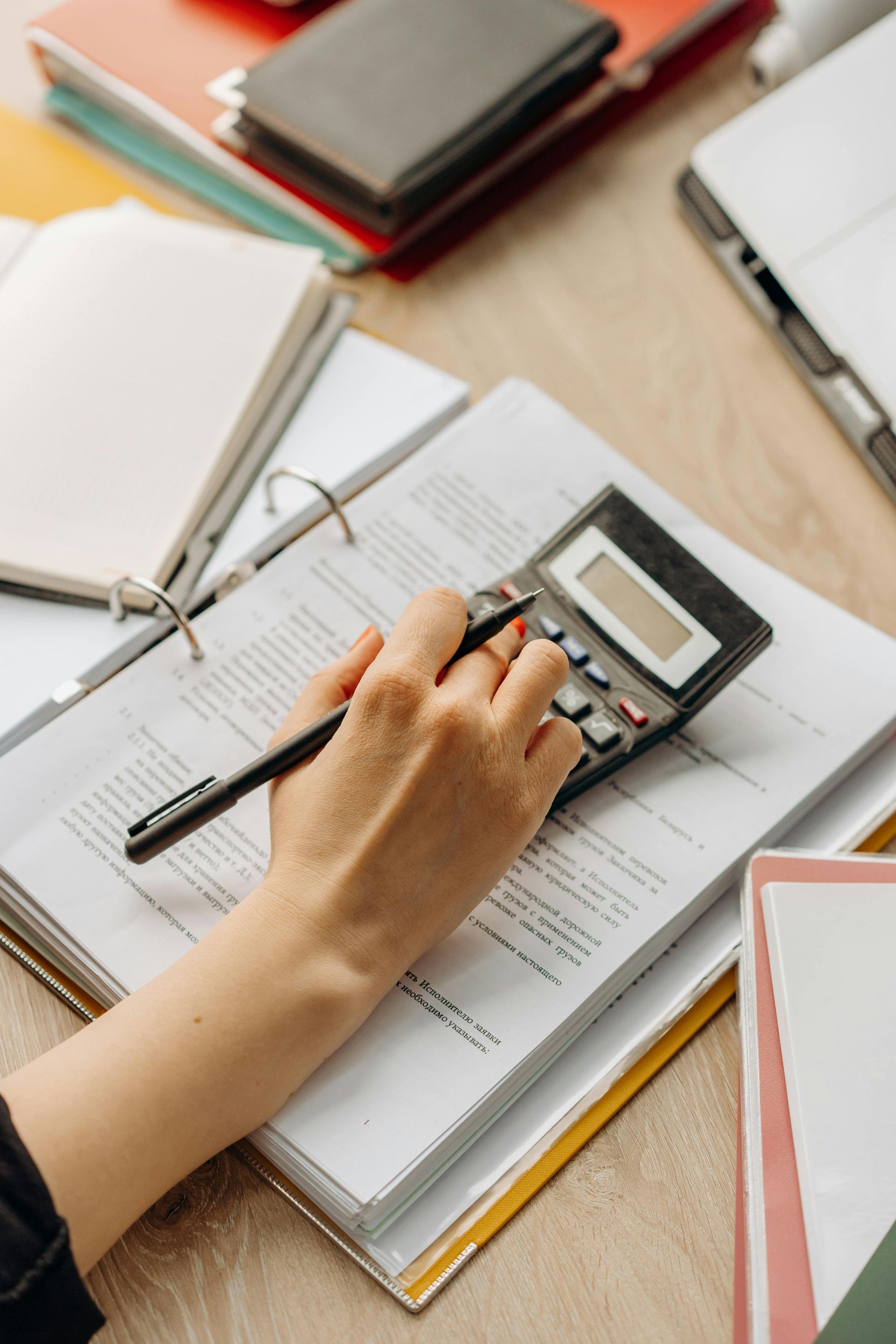 A person's hand using a calculator on paperwork surrounded by office supplies.