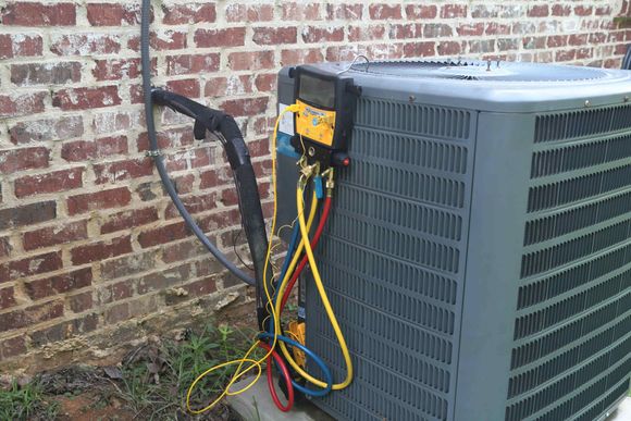 An air conditioner is being serviced by a brick wall.