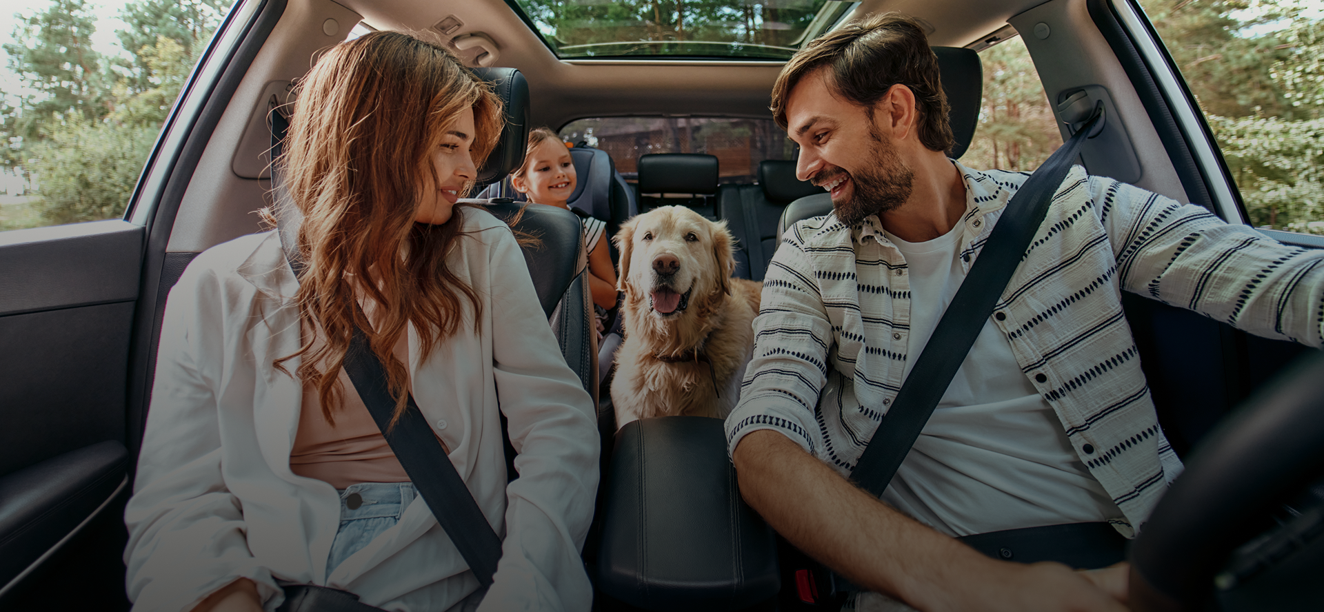 Two people and a dog sitting in a car, smiling at each other on a road trip | Golden Gear Automotive