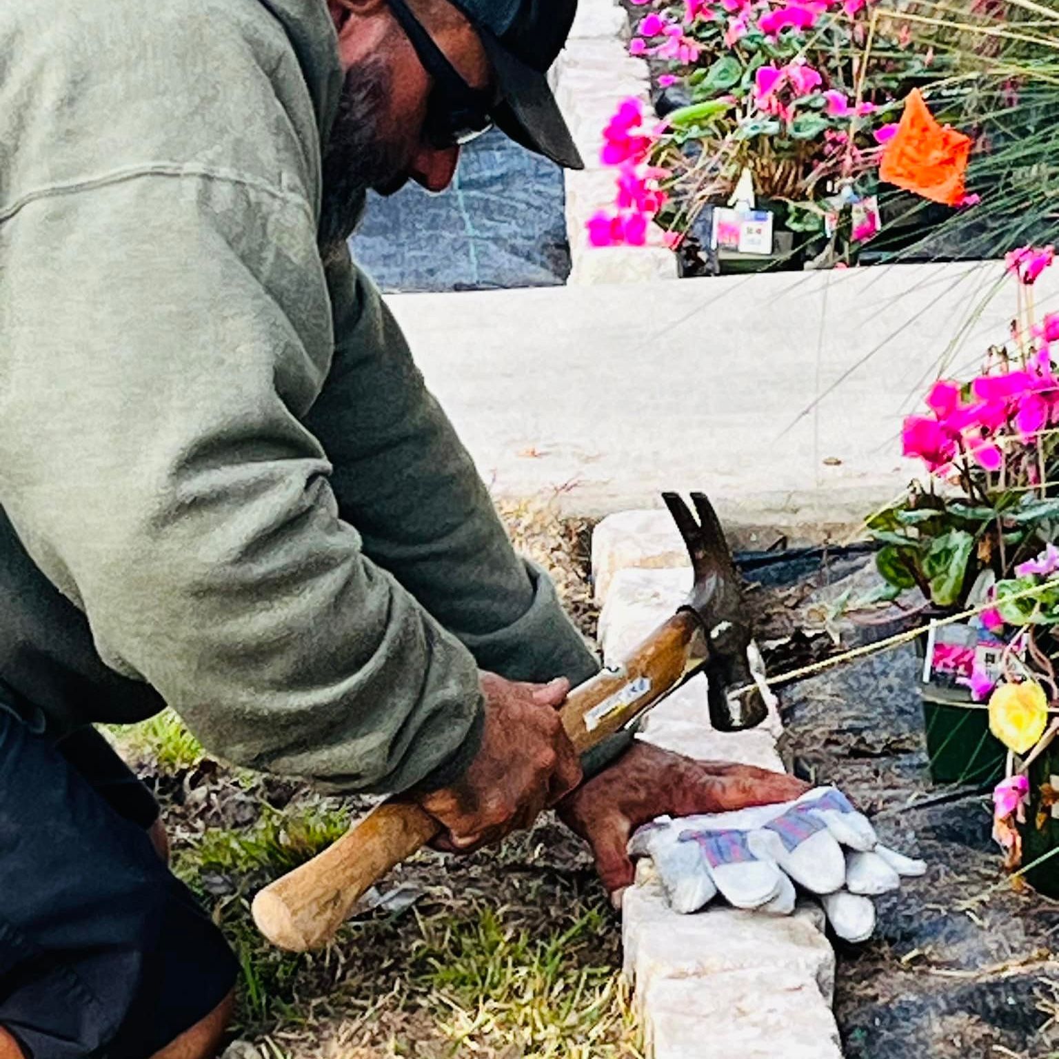 A man is working on a flower bed border with a hammer.