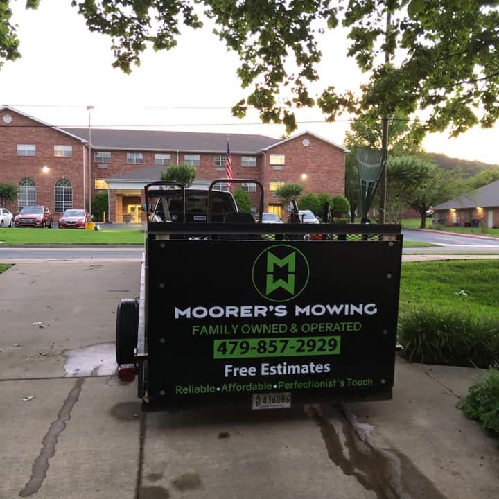 A mowing trailer is parked in front of a brick building