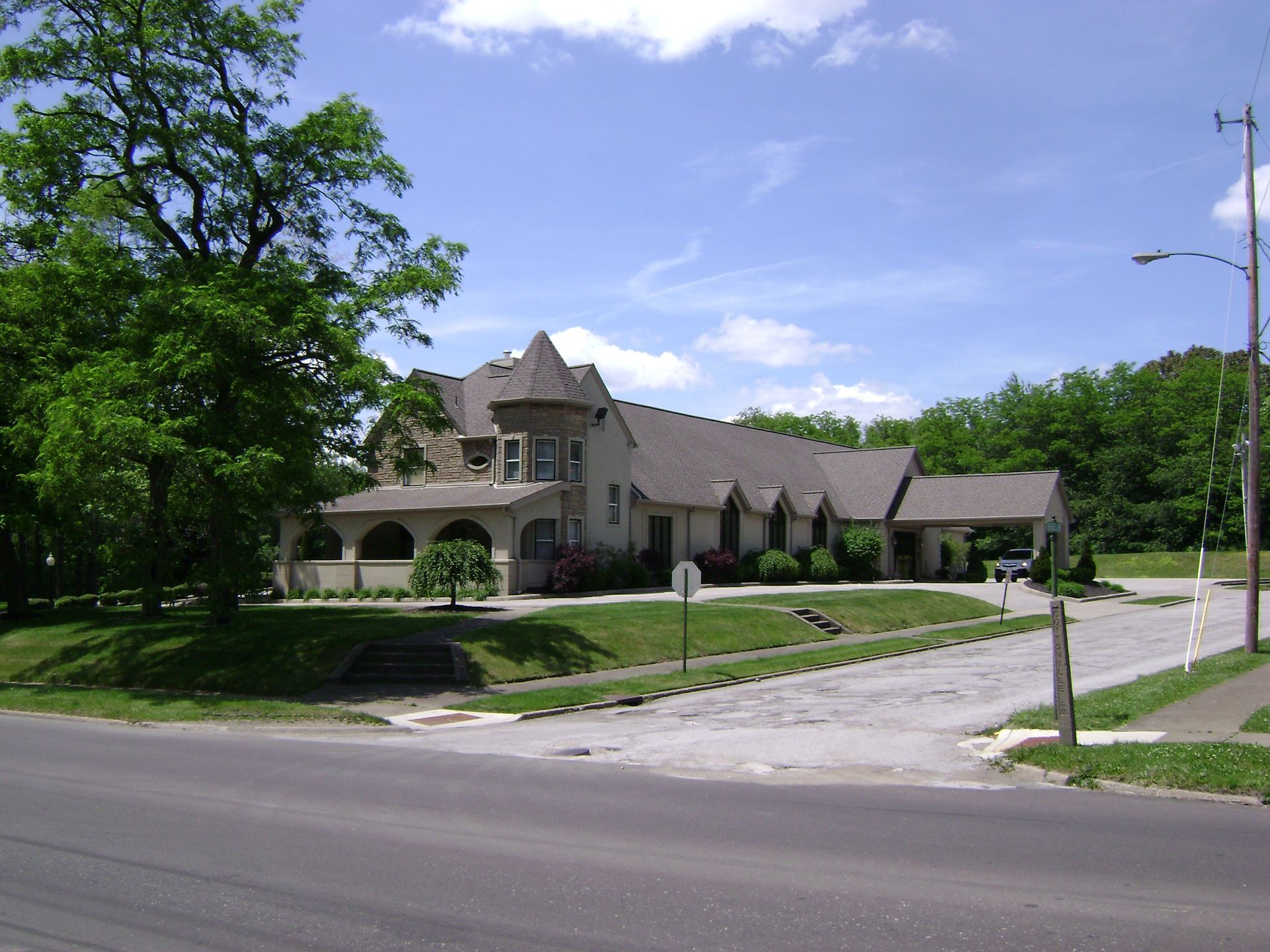 Large stone house with arched porch on a tree-lined street under a blue sky