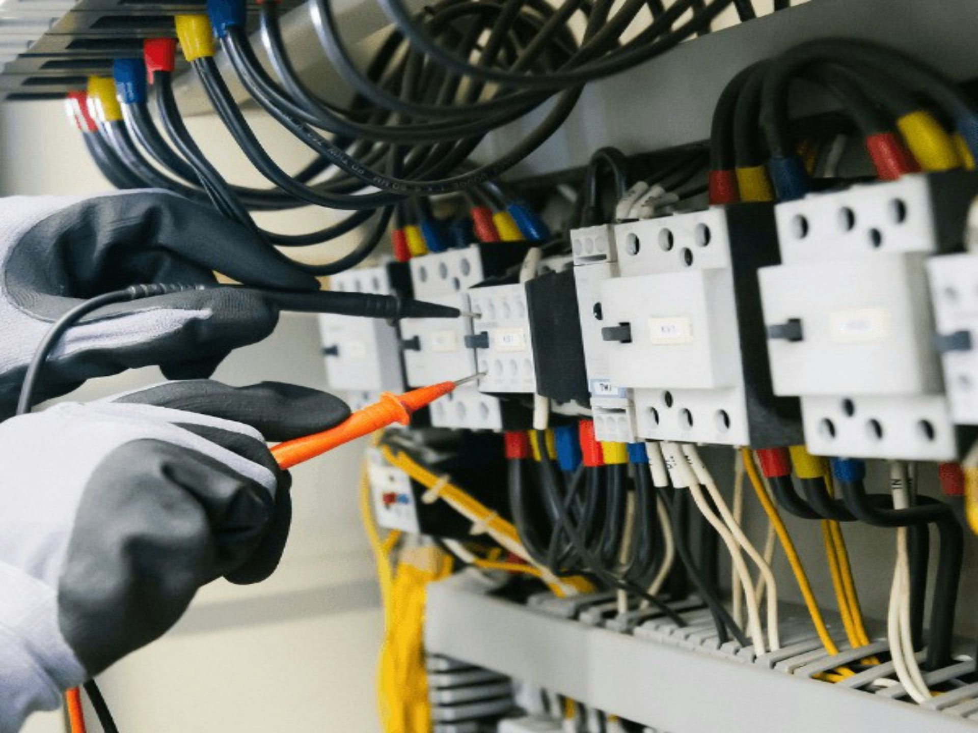 A technician in a hard hat and high-visibility vest inspects electrical equipment in an industrial cabinet.