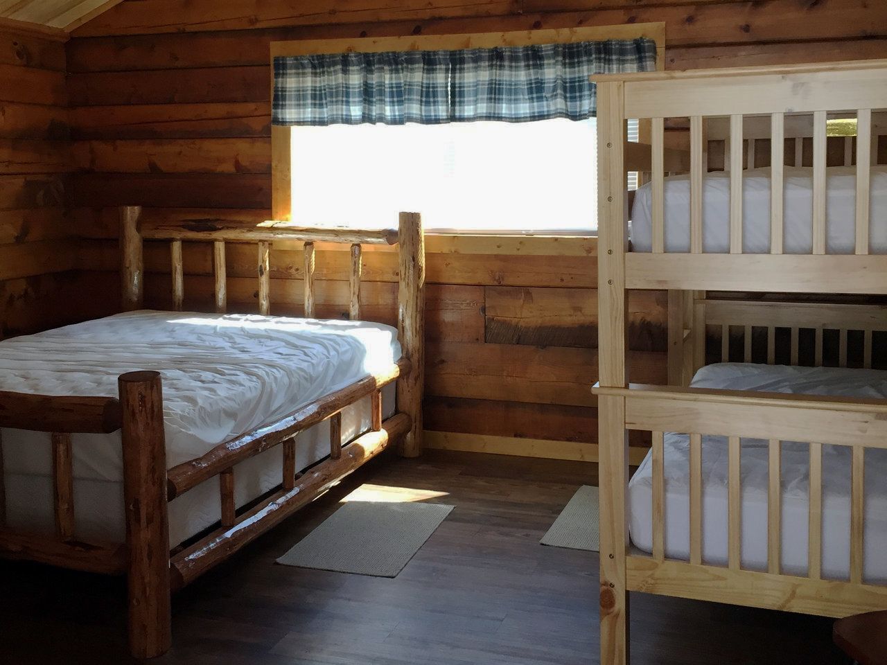 Log cabin bedroom with double bed, bunk bed, window, and wooden walls.