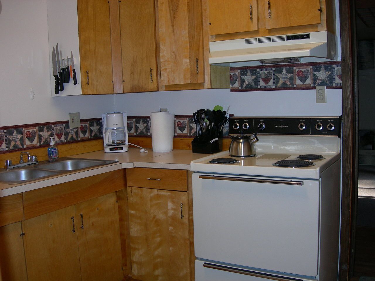 Kitchen with wood cabinets, white stove, and wallpaper border. Sink and appliances visible.