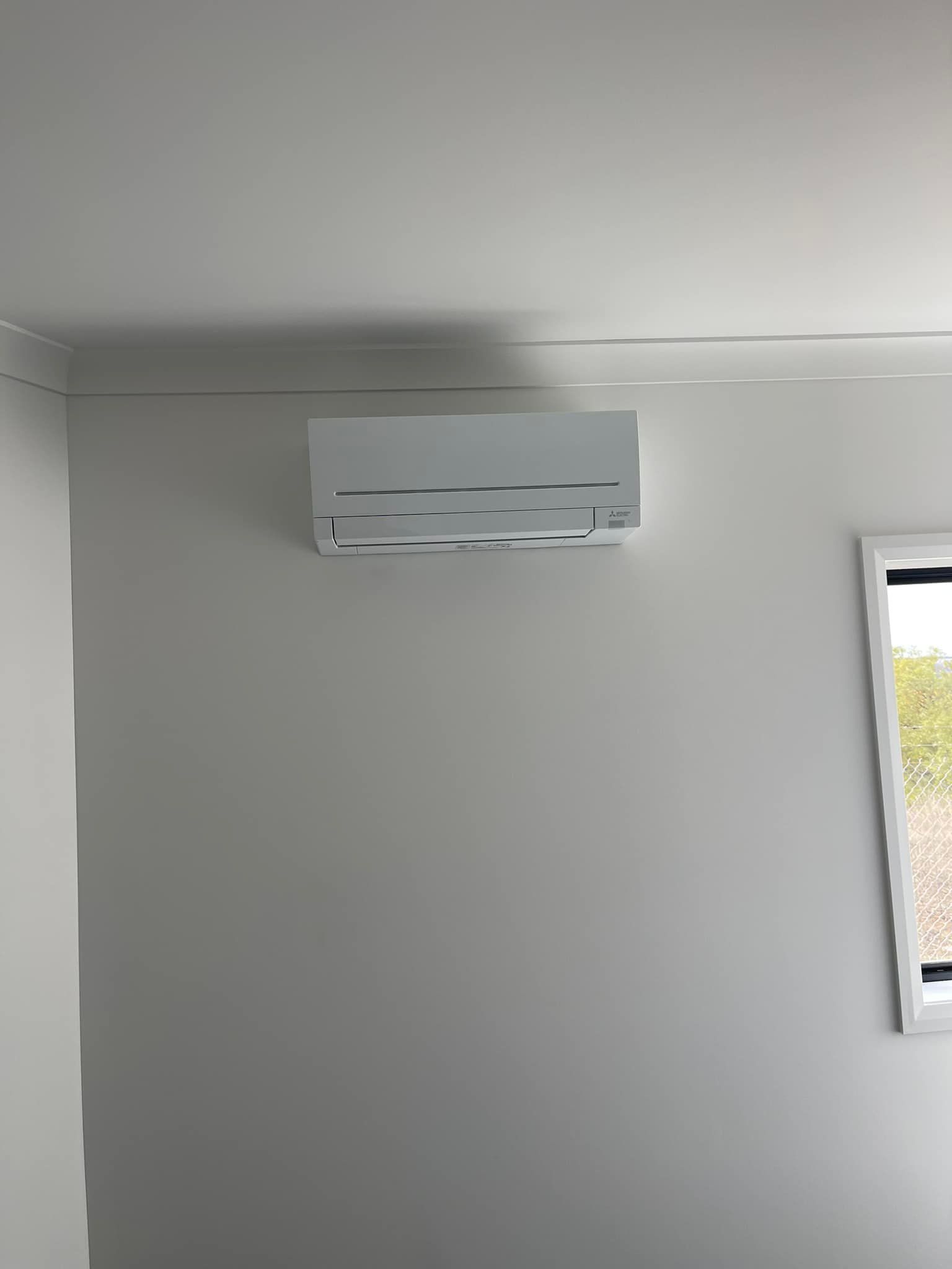 White Air Conditioning Unit on A Light Gray Wall Near a Window — Canobolas Air in Parkes, NSW